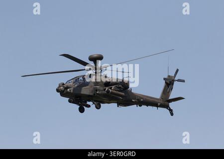 Un elicottero d'attacco militare AH-64 Apache con rotori rotanti vola attraverso un cielo nuvoloso e coperto con il suo carrello di atterraggio. Foto Stock