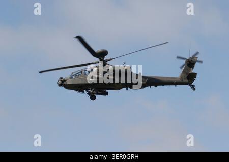 Un elicottero d'attacco militare AH-64 Apache con rotori rotanti vola attraverso un cielo nuvoloso e coperto con il suo carrello di atterraggio. Foto Stock