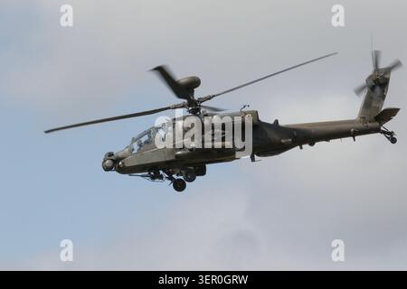 Un elicottero d'attacco militare AH-64 Apache con rotori rotanti vola attraverso un cielo nuvoloso e coperto con il suo carrello di atterraggio. Foto Stock