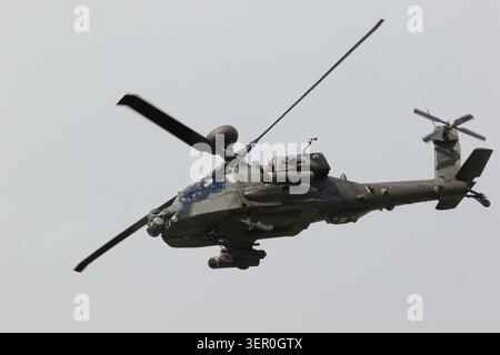 Un elicottero d'attacco militare AH-64 Apache con rotori rotanti vola attraverso un cielo nuvoloso e coperto con il suo carrello di atterraggio. Foto Stock