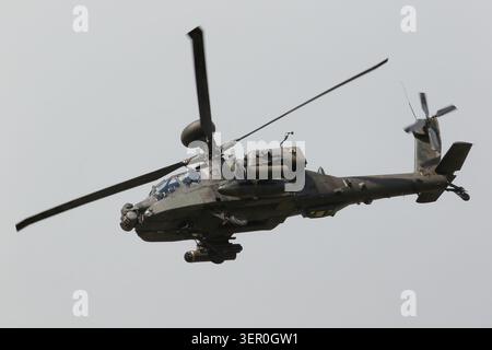 Un elicottero d'attacco militare AH-64 Apache con rotori rotanti vola attraverso un cielo nuvoloso e coperto con il suo carrello di atterraggio. Foto Stock