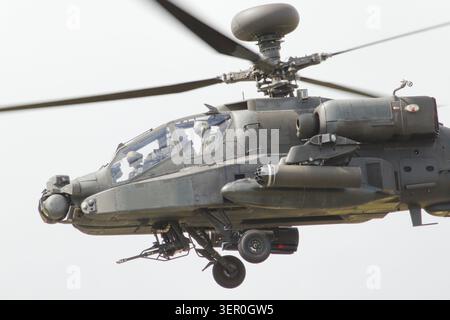 Un elicottero d'attacco militare AH-64 Apache con rotori rotanti vola attraverso un cielo nuvoloso e coperto con il suo carrello di atterraggio. Foto Stock