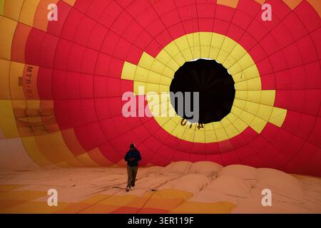 Interno della mongolfiera durante il gonfiaggio con una persona in piedi nanizzata all'interno della colorata busta rossa e gialla e della corona scura Foto Stock