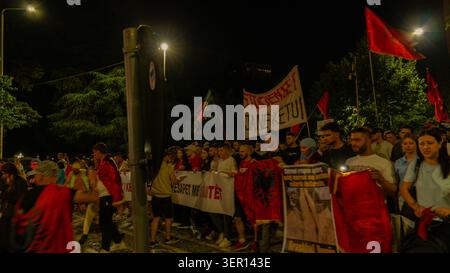 Tirana, Albania – 17 giugno 2026: I manifestanti stanno dietro gli striscioni e ondeggiano le bandiere albanesi durante una manifestazione serale a Tirana. Foto Stock