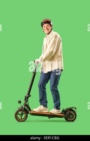 Uomo maturo con casco in sella a uno scooter elettrico su sfondo verde Foto Stock