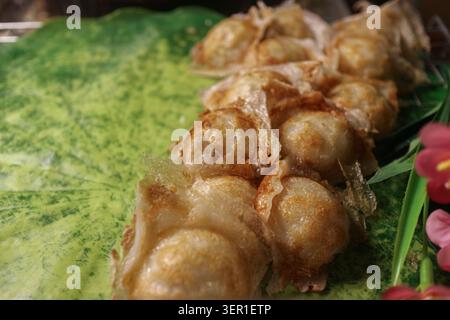 Dessert tradizionale thailandese da strada Kanom Krok, pancake al budino di cocco, serviti su una grande foglia di loto verde con spazio libero a sinistra, Thailandia. Foto Stock