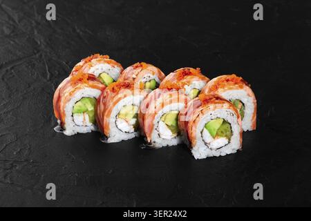 Sushi appena preparato con salmone, avocado e tobiko, splendidamente disposti su sfondo nero Foto Stock