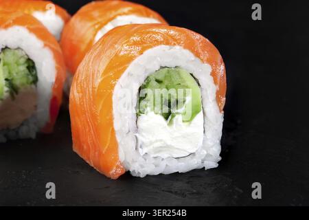 Primo piano di deliziosi panini di sushi uramaki philadelphia, con salmone, cetrioli e formaggio spalmabile, serviti su una superficie scura Foto Stock