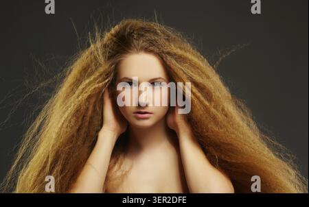 Ritratto di una giovane donna dai capelli rossi ricci che tocca i suoi lunghi capelli ondulati Foto Stock