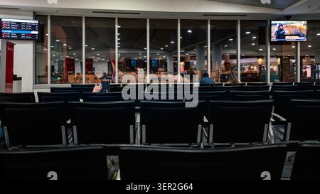 Vista notturna dell'area salotto del gate delle partenze, con i passeggeri in attesa e un aereo Qantas visibile attraverso le finestre, all'Aeroporto di Perth. Foto Stock