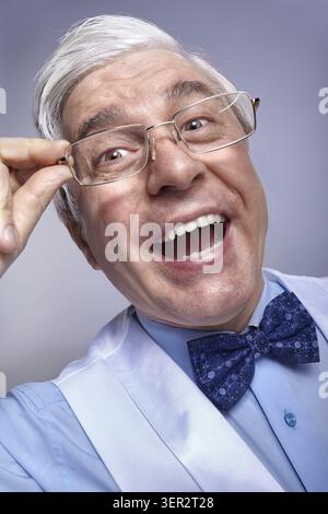 Close up ritratto di divertente sorriso allegro imprenditore senior addetto. Adulto uomo di mezza età con gli occhiali in mani in posa su uno sfondo grigio Foto Stock