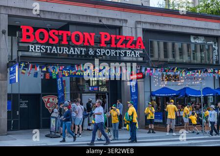 Vancouver, Canada - 13 giugno 2026: I tifosi di calcio con maglie gialle e verdi affollano l'ingresso al Boston Pizza e il suo umbrell nel patio della Coppa del mondo FIFA 2026 Foto Stock