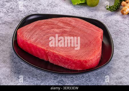 Bistecca di tonno crudo fresco su piatto nero con lime e spezie su fondo grigio. Pesce di alta qualità per preparazione di sushi o sashimi Foto Stock