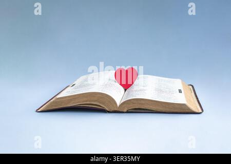 Cuore di carta rossa sulla cima del crocifisso a croce di legno. Isolato su sfondo chiaro. Foto Stock