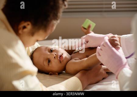 Black Mother che tiene il bambino durante il check-up pediatrico Foto Stock