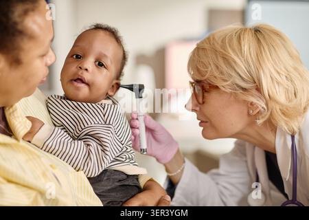 Madre nera che tiene in mano il bambino durante l'esame pediatrico dell'orecchio Foto Stock