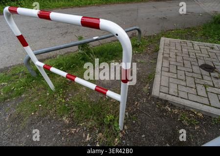 Una barriera si trova su una strada, impedendo l'accesso al veicolo. E' dipinto con strisce rosse e bianche ed e' posizionato vicino a un marciapiede e a una macchia d'erba. TH Foto Stock