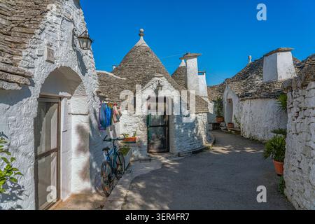 Case a trulli imbiancate con tetti conici in pietra e vasi in terracotta lungo un vicolo tranquillo, Rione Monti, Alberobello, provincia di Bari, Puglia, Italia Foto Stock