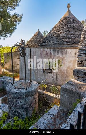 Case Trulli con tetti conici in pietra secca e un pozzo decorativo che rappresenta la tradizionale architettura italiana nel sud Italia. Puglia, Italia Foto Stock