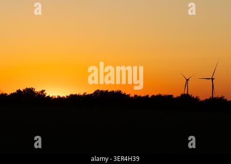 Un'ampia vista panoramica delle turbine eoliche che si stagliano contro un vasto cielo crepuscolo arancione al tramonto, con ampio spazio per le copie. Foto Stock