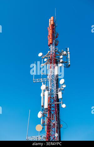 Torre di comunicazione cellulare con più antenne e piastre a microonde contro il cielo azzurro, moderna infrastruttura di telecomunicazioni Foto Stock