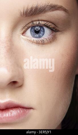 Primo piano macro ritratto di volto femminile e occhio blu. Donna umana mezza faccia con trucco di bellezza di giorno. Ragazza con pelle e lentiggini perfetti Foto Stock