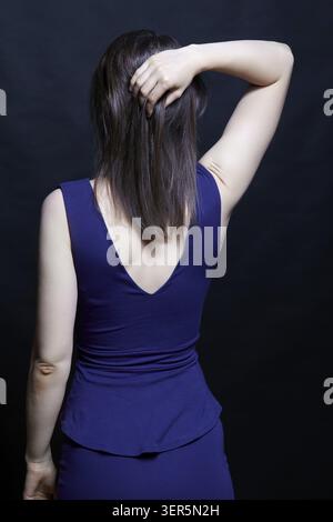 Giovane donna bruna in vestito blu. Vista femminile dal lato posteriore. Hamd in testa Foto Stock