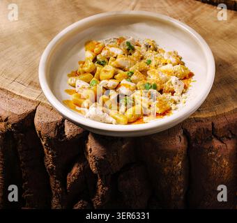 Un gustoso piatto di pasta comprende orecchiette e frutti di mare, guarniti con cipolle verdi. Il rustico tavolo in legno aggiunge calore a questa invitante creazione culinaria, perfetta per cene informali. Foto Stock