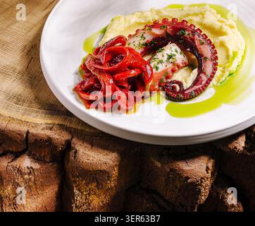 Un piatto splendidamente placcato con polpo grigliato su crema di patate, guarnito con peperoni rossi e un filo di salsa verde. Perfetto per gli amanti del pesce e per i pasti gourmet. Foto Stock