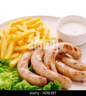 Tre salsicce grigliate sono posizionate su un piatto bianco. Accanto alle salsicce, ci sono patatine fritte e una piccola ciotola di salsa. La lattuga verde è sotto le salsicce. Foto Stock