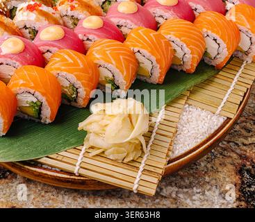 Rotoli di sushi colorati sono ordinati su un tappetino in bambù, con vari ingredienti. I panini rosa, arancione e rosso sono disposti in modo accattivante con lo zenzero sottaceto. Foto Stock