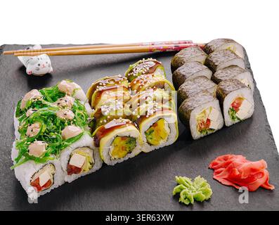 Vari sushi roll sono disposti ordinatamente su un piatto nero. Alcuni panini hanno verdure e frutti di mare, mentre lo zenzero sottaceto e il wasabi sono posizionati di lato. Foto Stock