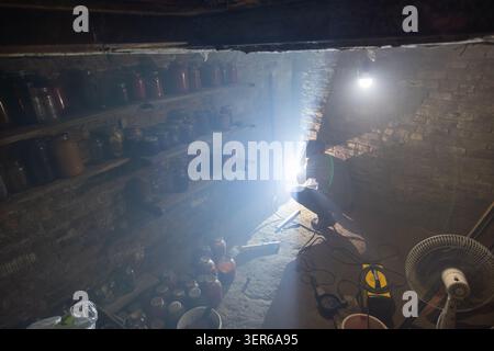 La persona si impegna attivamente nella saldatura all'interno di un seminterrato scarsamente illuminato. La luce intensa della saldatura illumina l'ambiente circostante riempito di attrezzi e vaschette. Foto Stock