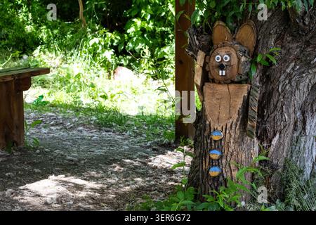 Una divertente scultura di animali scolpita da tronchi decora un campo ombreggiato lungo il fiume. La luce soffusa sulle foglie e sui grani di legno crea un'atmosfera rustica e amichevole Foto Stock