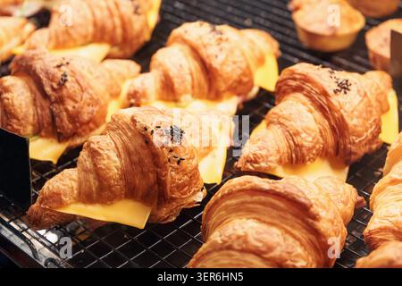 Croissant appena sfornati con ripieno di prosciutto e formaggio, conditi con semi di sesamo nero, esposti su una griglia refrigerante Foto Stock