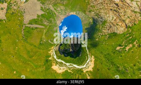 La vista aerea cattura il vasto paesaggio montano caratterizzato da scogliere rocciose e verdi colline ondulate. Inverte la proiezione del piccolo pianeta. Valle tranquilla con rive Foto Stock