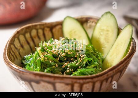 Insalata di alghe wakame, condita con semi di sesamo e guarnita con cetriolo a fette in un recipiente di ceramica Foto Stock