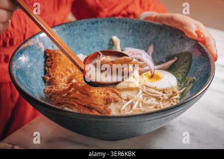 Persona in possesso di una ciotola di ramen cremoso tonkotsu con katsu di pollo, uova, funghi e germogli di soia Foto Stock