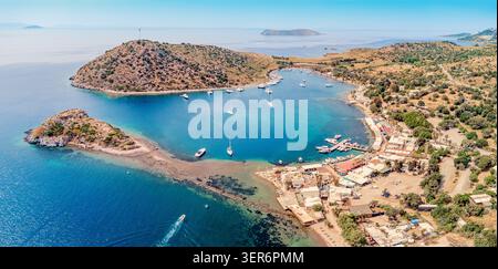 Vista aerea della baia di Gumusluk che mostra le barche nel mare turchese dell'Egeo con il piccolo villaggio di pescatori e le isole circostanti a Turkiye Foto Stock
