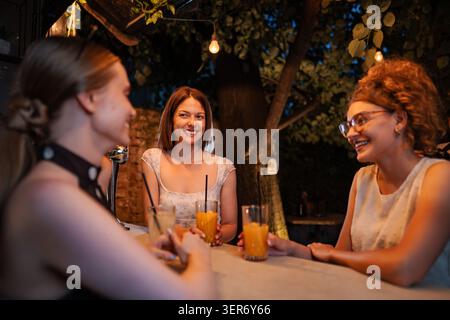 Tre amiche donne che ridono e socializzano al bar all'aperto Foto Stock