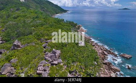 Stupefacente ripresa aerea che cattura la bellezza selvaggia di Anse Cocos alle Seychelles, mostrando chiare onde turchesi dell'oceano che si infrangono contro le pietre di granito Foto Stock
