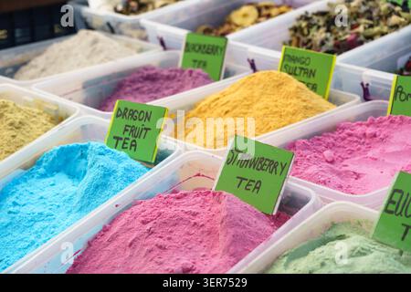 Vivaci tè in polvere in contenitori trasparenti in un mercato, etichettati con nomi come tè alla frutta del drago e tè alle fragole, evidenziando vari colori e. Foto Stock
