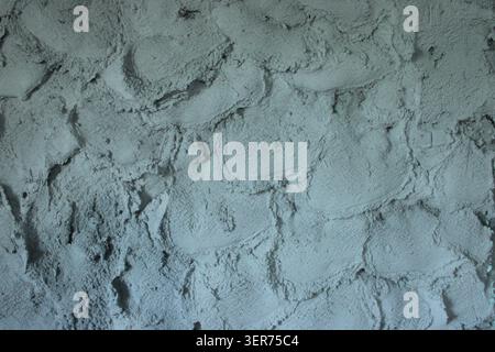 Una parete mostra una consistenza ruvida fatta di cemento in diverse tonalità di grigio. La superficie presenta motivi e forme naturali derivanti dal processo di costruzione. Foto Stock