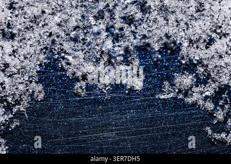 Macrofotografia di splendidi cristalli di ghiaccio e fiocchi di neve su una superficie blu graffiata Foto Stock