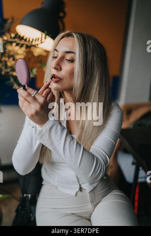 Donna d'affari che applica il rossetto allo specchio della scrivania per preparare una riunione in un ufficio moderno Foto Stock