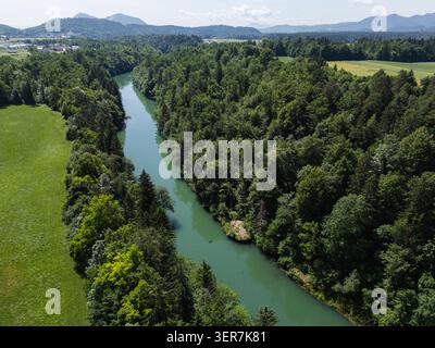 Un fiume scorre attraverso una lussureggiante foresta verde in un ambiente naturale sotto un cielo blu. L'area mostra segni di attività all'aperto e bellezza. Foto Stock