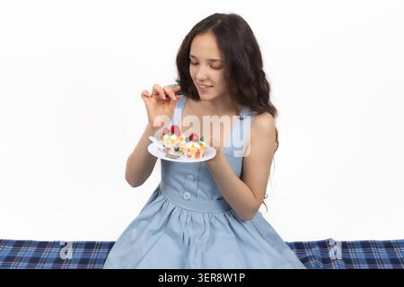Giovane donna felice seduta su una coperta e che mangia dolci dolci Foto Stock