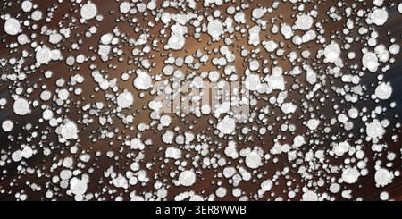 Uno sfondo artistico astratto caratterizzato da numerose particelle circolari bianche, testurizzate sparse su uno sfondo sfumato marrone scuro e bronzo. Foto Stock