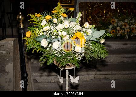 Composizione floreale con girasoli, rose e vegetazione che creano un'atmosfera celebrativa in una chiesa Foto Stock