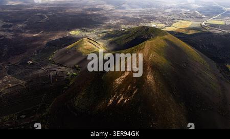 Vista aerea dei coni vulcanici di Lanzarote e dei campi di frassino nero, dove le viti crescono in pozzi murati di pietra, immersi in una luce magica e in una spettacolare ombra Foto Stock